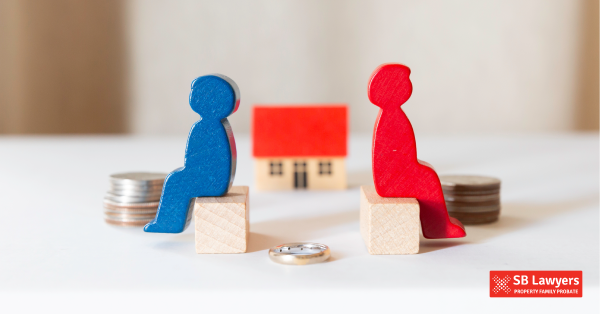 Two wooden figurines, one red and one blue, facing away from each other and a wedding ring in the middle. SB Lawyers is your go to for divorce solicitors